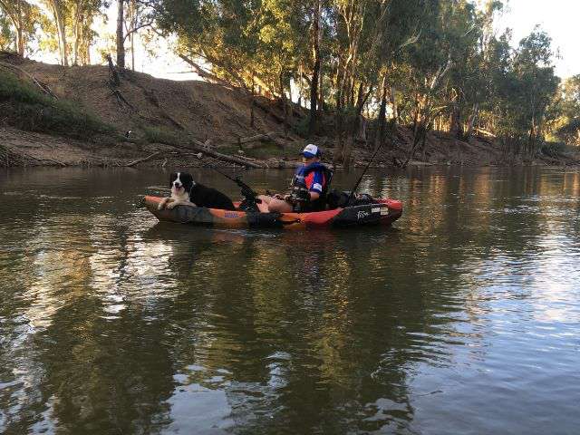 A photograph of a young man and a border collie in a kayak fishing on a river.